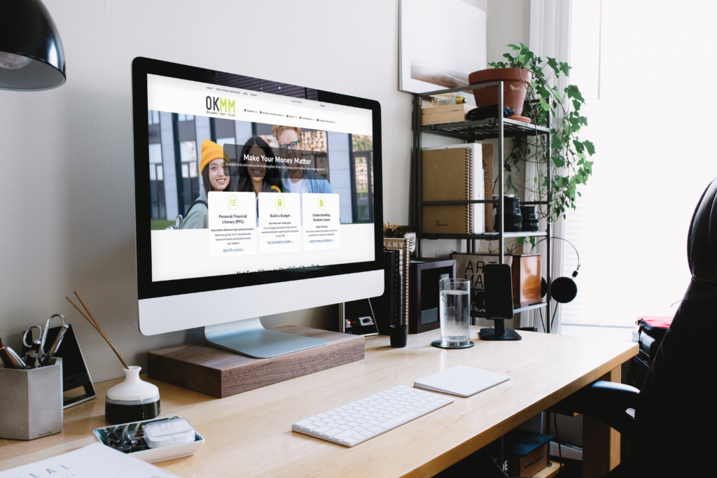Oklahoma Money Matters website homepage displayed on a desktop computer in a modern workspace.
