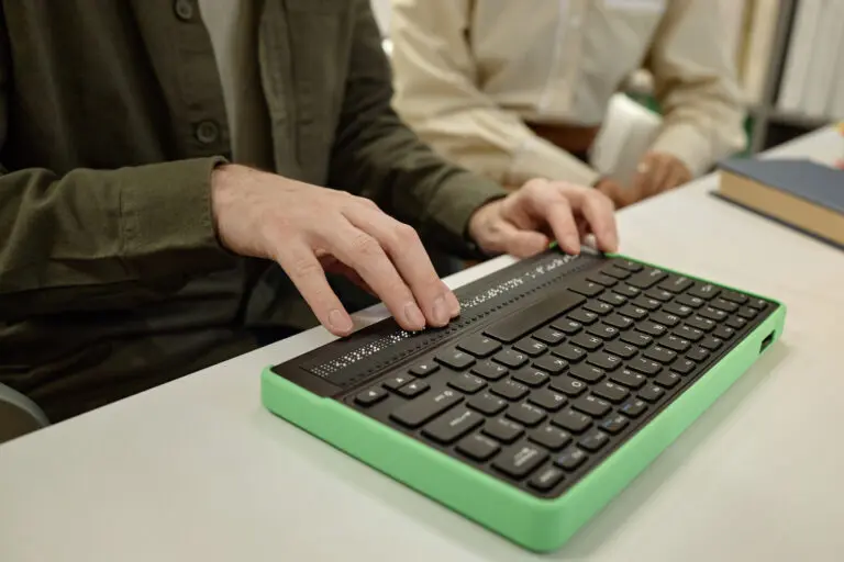 Young Man Using Braille Keyboard While Reading Book in Library